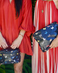 Two women holding black pouch bags with butterfly pattern, one in a red dress and the other in a striped dress.