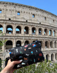 Black pouch with colorful landmark designs held in front of the Colosseum in Rome.