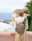 Woman standing in front of Italy coastline wearing shimmer bronze crossbody backpack
