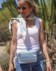 Woman standing in sun wearing a shimmer ice blue puffer crossbody fanny pack belt bag