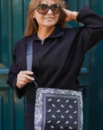 Woman wearing sunglasses and a black outfit with a bandana patterned bag, standing against a green door.