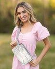 Woman in a pink dress holding a gray crossbody bag with gamma phi beta greek letters embroidered on the bag.