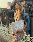 Woman holding a pouch with 'LOVE' on it, standing on a rooftop with cityscape in the background