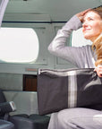 Woman seated in an airplane doorway holding a black jumbo zipper pouch with silver and pewter center stripes.