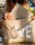 Person holding a beige bag with 'LOVE' printed on it, outdoors.
