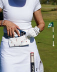 Person on a golf course holding a golf club and a fanny pack with golf-themed designs.