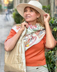 Woman wearing a wide-brimmed hat, orange sweater, and beige puffer tote on a city street.
