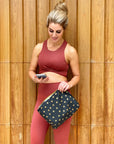 Woman in workout clothing using a zipper pouch in black with gold stars for her phone and essentials