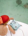 Woman with a sea green turtle patterned zipper pouch overlooking sea turtles in ocean