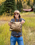 Woman holding a Shimmer Bronze Medium Zipper Pouch with metallic gold heart, moon, and star print in a grassy outdoor setting