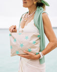 Woman standing by the ocean with a beige and green stars clutch bag