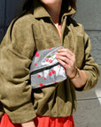 Person holding a silver pouch with red cherry design against a gray wall.