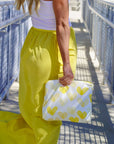 Person wearing yellow pants holding a white clutch with yellow hearts on a blue metal bridge.