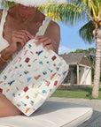 Person holding a landmark patterned pouch outdoors with palm trees and a building in the background