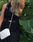 Woman in a black dress holding a white clutch against a green leafy background