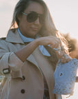 Woman in a beige coat holding a blue bandana pouch with a blurred background