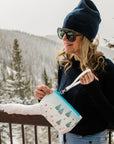 Woman carrying bluebird skier and snowboarder wristlet in snow