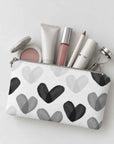Mini zip pouch in black and white heart print containing various makeup items on light gray background.