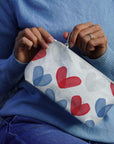 Person holding a pouch with red and blue heart patterns against a blue sweater background