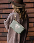 Woman wearing mini green zipper pouch with heart and clip on wristlet strap