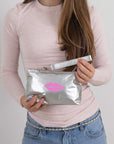 Person holding a silver wristlet with a pink lip print on a plain background