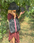 Woman standing next to olive tree in burgundy dress with a black and burgundy stripe wine tote