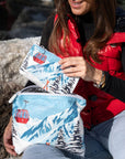 Woman placing a matching mini red gondola print pouch into a medium zipper pouch featuring a snowy mountain landscape and ski gondola design.