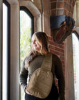 Woman standing near brick wall wearing shimmer bronze crossbody backpack