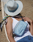 Woman laying on a hammock wearing a shimmer ice blue puffer crossbody fanny pack belt bag