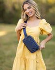 Girl in yellow dress wearing Puffer Crossbody Fanny Pack Belt Bag in Shimmer Navy Blue