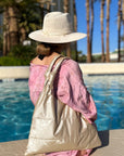 Woman sitting at edge of pool with shimmer beige puffer tote handbag on shoulder