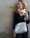 Woman wearing crossbody purse in silver standing against concrete wall