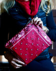 Woman wearing red scarf holding a red bandana patterned zipper clutch bag