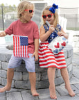 Kids outdoors in red, white, and blue holding a wristlet and American flag
