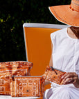 Woman sitting outdoors with orange bandana patterned bags and a hat