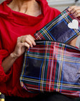 Person in red shirt holding set of two pouches in tartan plaid pattern, smaller pouch features white heart against blurred background.