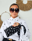 Woman wearing a matching black scarfette on her wrist with a mini zipper pouch with white hearts, moons and stars pattern.