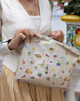 Close up of woman holding a shimmer beige medium zipper pouch with lemon, grapes, pizza, statue, wine glass pattern