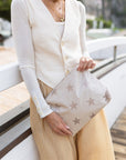 Woman in white sweater and striped pants holding a shimmer beige with stars zipper pouch