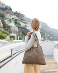 Woman on the coast in Italy wearing a shimmer bronze purse over shoulder