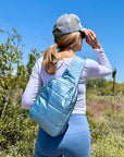 Woman outside wearing blue pants and shimmer ice blue crossbody backpack