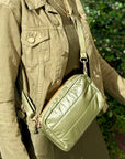 Woman wearing green dress, jacket, and shimmer olive green crossbody puffer purse