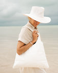 Woman on a beach with white hat and shimmer white puffer purse tote on shoulder