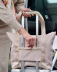 Person unzipping trolly sleeve pockeet on signature travel tote bag in beige