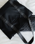 Close-up of the black signature tote's striped strap laid flat beside the matching signature patterned pouch.