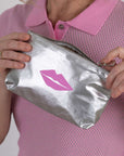 Person holding a silver pouch with a pink lip design on a white background