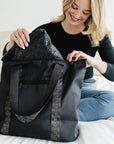 Woman kneeling on a bed unpacking the black signature travel tote.