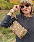 Woman wearing a bronze metallic wristlet pouch with gold heart, moon, star design outside in the fall.
