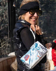 Two women holding hands and coordinating zipper pouches with a red gondola and snowy mountain print while relaxing at a ski resort.