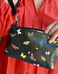 Person holding a black pouch with butterfly designs against a red garment background